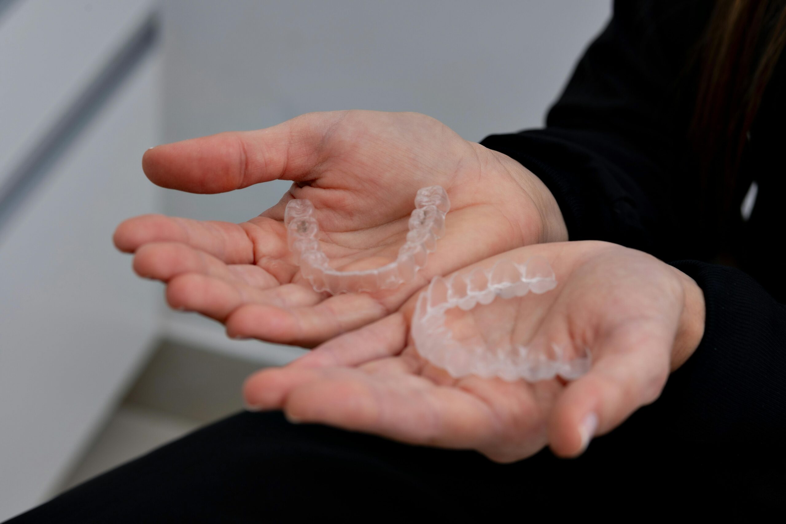 pexels-photo-28407748-28407748 Close-up of hands holding clear dental aligners in a dental clinic setting.